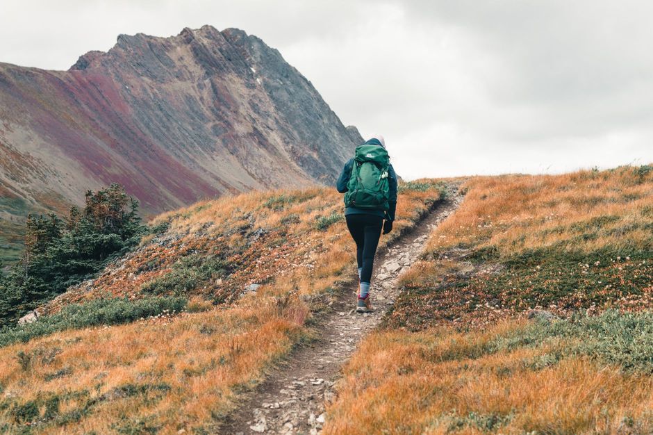 A hiker with a backpack walking a mountain trail in fall light