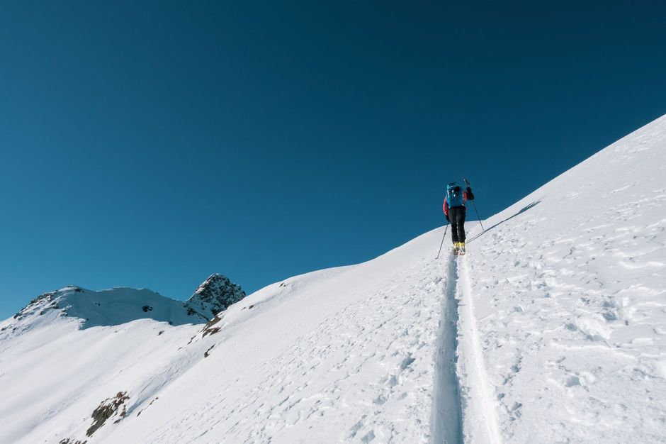 A backcountry skier skinning uphill on a sunny snow-covered ridge