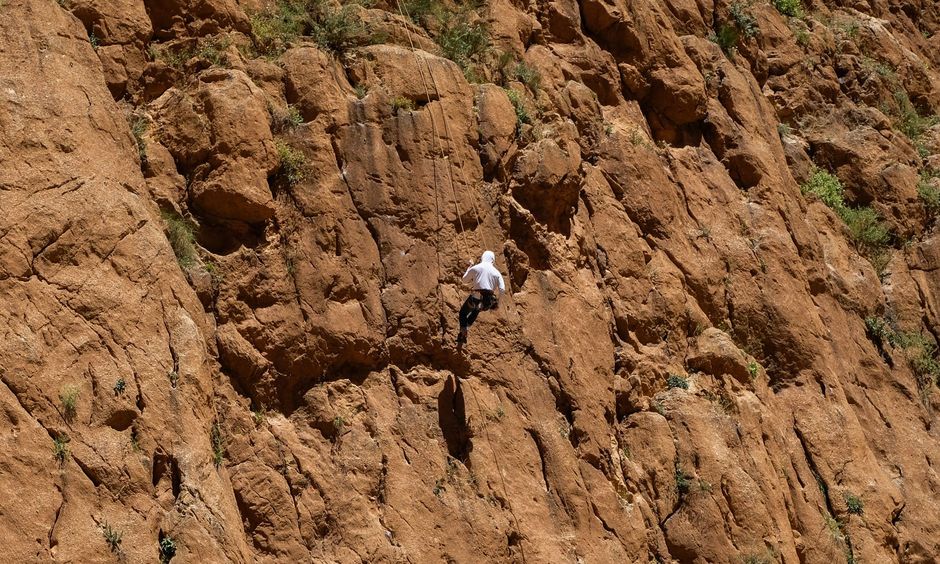 A climber ascending a sunlit rock face on a rope