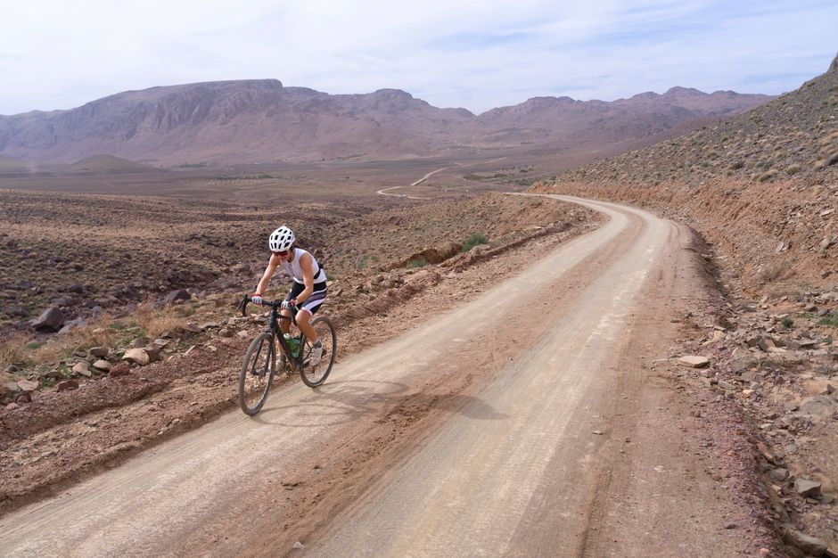 A cyclist riding a gravel bike on a remote dirt road through desert mountains
